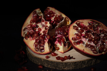 Pomegranate fruit cut in half on a rustic wooden log on a dark background. Reddish tropical fruit...