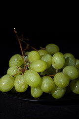 Vertical image of a bunch of green grapes on a black plate on a dark background. Round and juicy fruit
