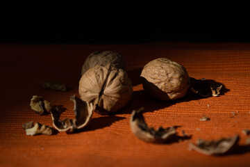 Walnuts scattered on a rustic orange tablecloth on a dark background. Edible seed nut