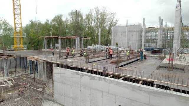 Builders engaged in construction process around reinforced concrete structures and steel reinforcement bars. Lifting crane at background assisting with material handling