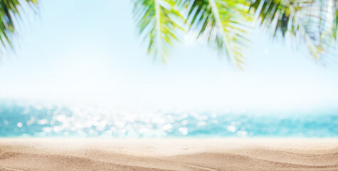 A tranquil seaside landscape with soft-focus palm leaves in the foreground and a golden sandy beach...