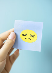 hand holding blue sticky note with sad emoji, expressing emotions