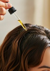 Fototapeta premium Woman applying hair oil with dropper to brown hair for nourishment and shine