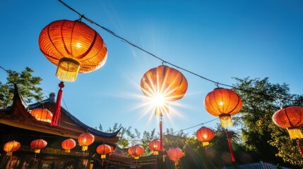 Bright sun shines through orange lanterns strung against a clear blue sky.