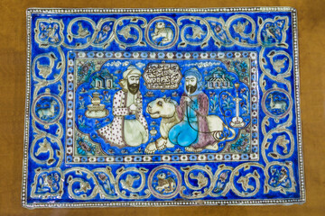 A decorative Persian glazed tile from the 19th century. The design depicts two men relaxing and a lion. The men are drinking tea and smoking a hookah. Shot in Isfahan, Iran