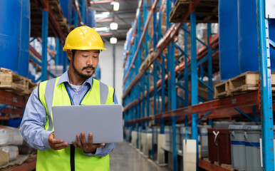 Warehouse worker in hard hat using laptop, managing inventory efficiently