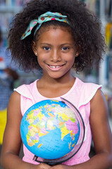 Fototapeta premium Exploring geography, girl holding globe in school library, smiling brightly