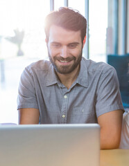 Smiling man using laptop in cafe, enjoying relaxed work environment