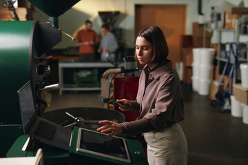 High angle shot of serious businesswoman launching professional and massive coffee roaster machine while her partners discussing coffee in blurred background
