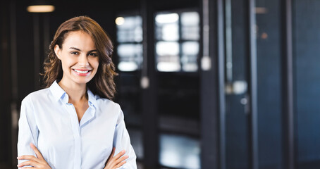 Confident businesswoman smiling in modern office, arms crossed, looking professional, copy space