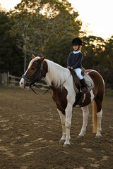 A young girl rider in a helmet and equestrian boots sits on her beloved horse at the stable,...