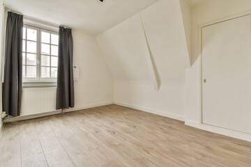 A spacious room featuring minimalistic design with white walls, wooden flooring, and large windows allowing for ample natural light.