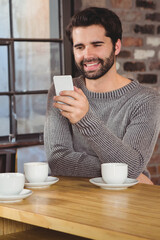 Smiling man using smartphone at cafe table with coffee cups