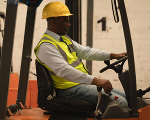 Warehouse worker driving forklift, wearing safety vest and helmet, focused on task