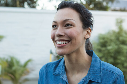 Wearing denim shirt, woman outdoors under sun with joyful expression