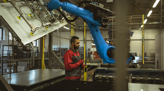 Engineer monitoring robotic arm in modern factory, ensuring efficient production