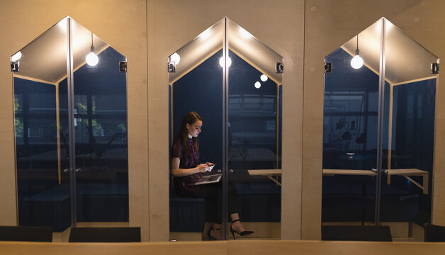 Young woman working on laptop in modern office booth, focused and productive, copy space