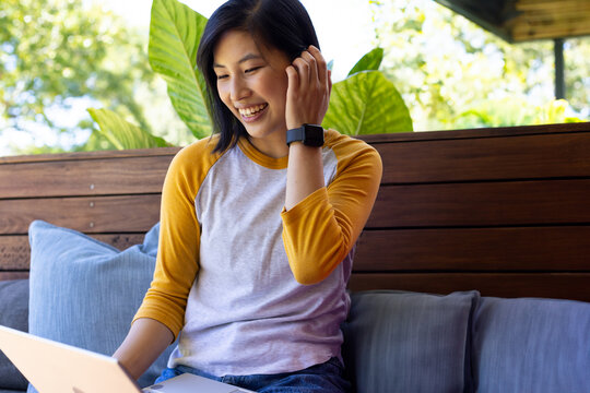 Smiling woman using laptop outdoors, enjoying leisure time on patio