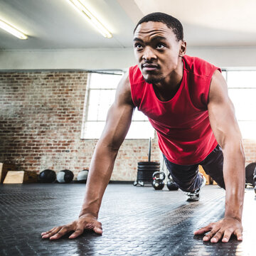 Man in red shirt doing push-ups in gym, focused and determined