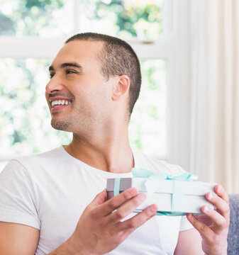 Smiling man holding gift box at home, enjoying special moment together