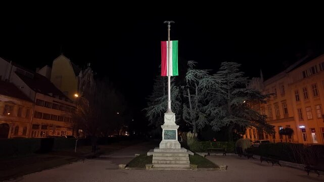 Illuminated Hungarian flag of loyalty in downtown Sopron at night, stands in a quiet city park. A serene atmosphere surrounds the monument with a historical vibe.