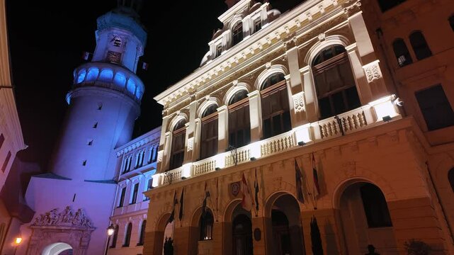 Nighttime view of the Main Square in Sopron, showcasing the illuminated Fire Tower and the Council building with vibrant lights.