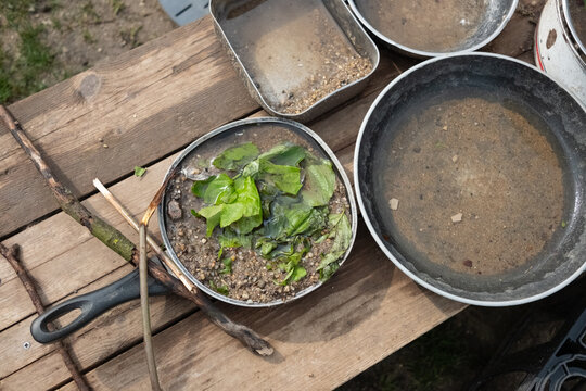 A lively mud kitchen in a kindergarten where children engage in free play, using pots, pans, and plates filled with sand, water, mud, and leaves. Montessori-inspired hands-on learning.