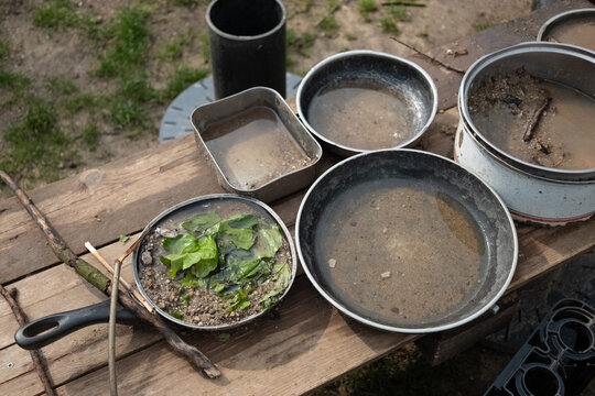 A lively mud kitchen in a kindergarten where children engage in free play, using pots, pans, and plates filled with sand, water, mud, and leaves. Montessori-inspired hands-on learning.