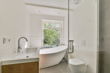 A sleek modern bathroom featuring a freestanding bathtub, minimalist design, and natural light streaming through a window, creating a serene atmosphere.