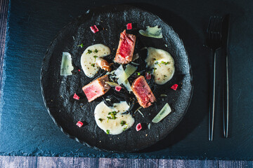 Tuna steak with white sauce, vegetables and spaghetti on a black plate. Restaurant serving of dishes, Mediterranean food.