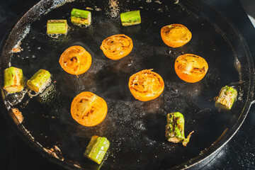 Yellow cherry tomatoes and asparagus are fried in a cast iron pan. Selected focus.