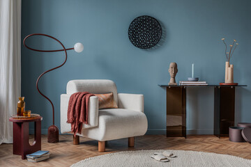 A cozy reading nook with a plush cream-colored armchair, a sculptural floor lamp, and warm textile accents, set against a bold blue wall for a modern yet inviting atmosphere.
