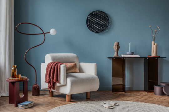 A cozy reading nook with a plush cream-colored armchair, a sculptural floor lamp, and warm textile accents, set against a bold blue wall for a modern yet inviting atmosphere.