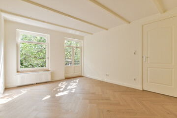 A spacious and airy interior with large windows allowing natural light. The light wood flooring and neutral walls create a serene atmosphere.