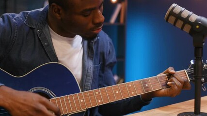 Playing acoustic guitar. Man is doing podcast in the studio.