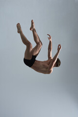 A male dancer in black shorts is captured mid-air in a falling motion, isolated on a light...
