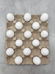 Sixteen white eggs resting in cardboard container on gray background easter