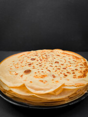 Stack of pancakes resting on dark background for pancake day breakfast maslenitsa or shrove tuesday with copy space