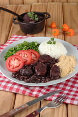 Comida tipica brasileira:  feijoada com acompanhamentos, servida no prato e na tigela