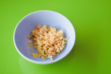 a bowl of finely minced light-colored food, like ginger or garlic, set against a bright green backdrop. The contrast helps the minced pieces stand out clearly.