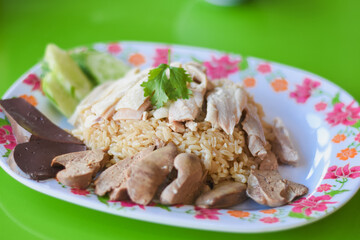 there are slices of chicken breast arranged neatly on a bed of rice. Surrounding the chicken and rice, you can see slices of cucumber, pieces of liver, and other organ meats.