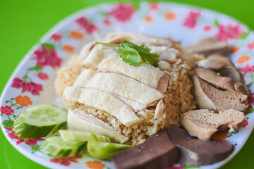 there are slices of chicken breast arranged neatly on a bed of rice. Surrounding the chicken and rice, you can see slices of cucumber, pieces of liver, and other organ meats.