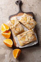 Homemade Orange Puff Pastry Pie with walnuts, raisins and fresh fruits filling close-up on wooden board on table. Vertical top view from above