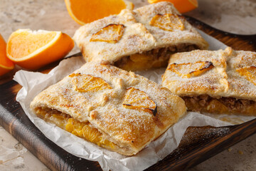 Homemade orange puff pastry pie with walnuts, raisins and fresh fruits close-up on wooden board on table. Horizontal