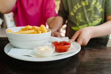 Kids eating french fries with mayonnaise and ketchup. Popular street junk food or snack.