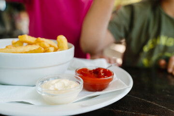 Kids eating french fries with mayonnaise and ketchup. Popular street junk food or snack.
