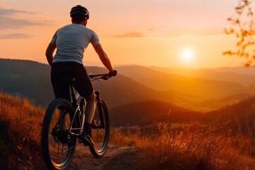 Cyclist watching golden sunset over mountain valley on top of hill
