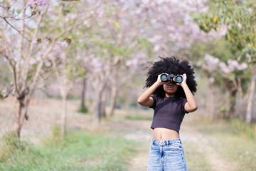 A young woman with voluminous curly hair explores nature using binoculars. Dressed in a black crop...