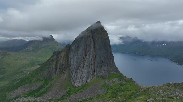 Drone footage of Segla rocky mountain and a lake behind clouds on Senja Island in Norway