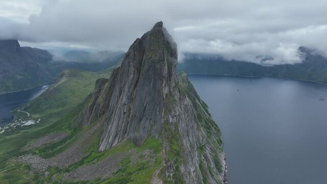 Drone footage of Segla rocky mountain and a lake behind clouds on Senja Island in Norway